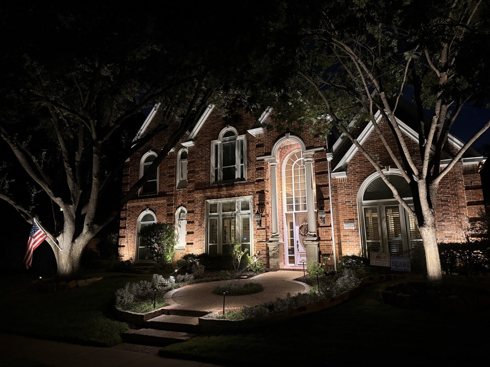 Brick two storey home at night with uplighting on the facade and the surrounding trees